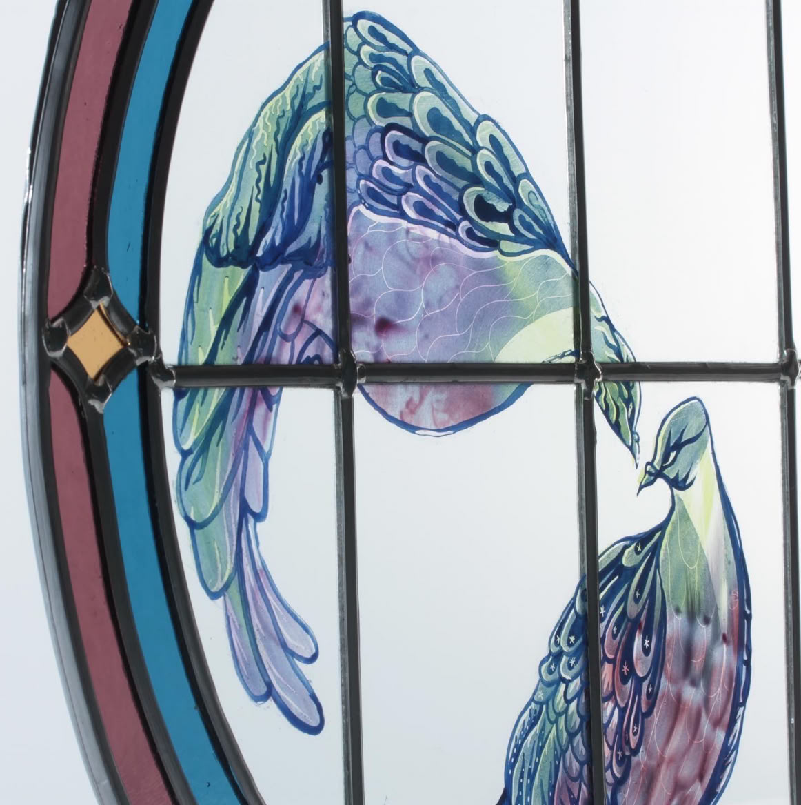 Stained glass window depicting two colorful birds facing each other, with a circular border and a diamond-shaped detail.